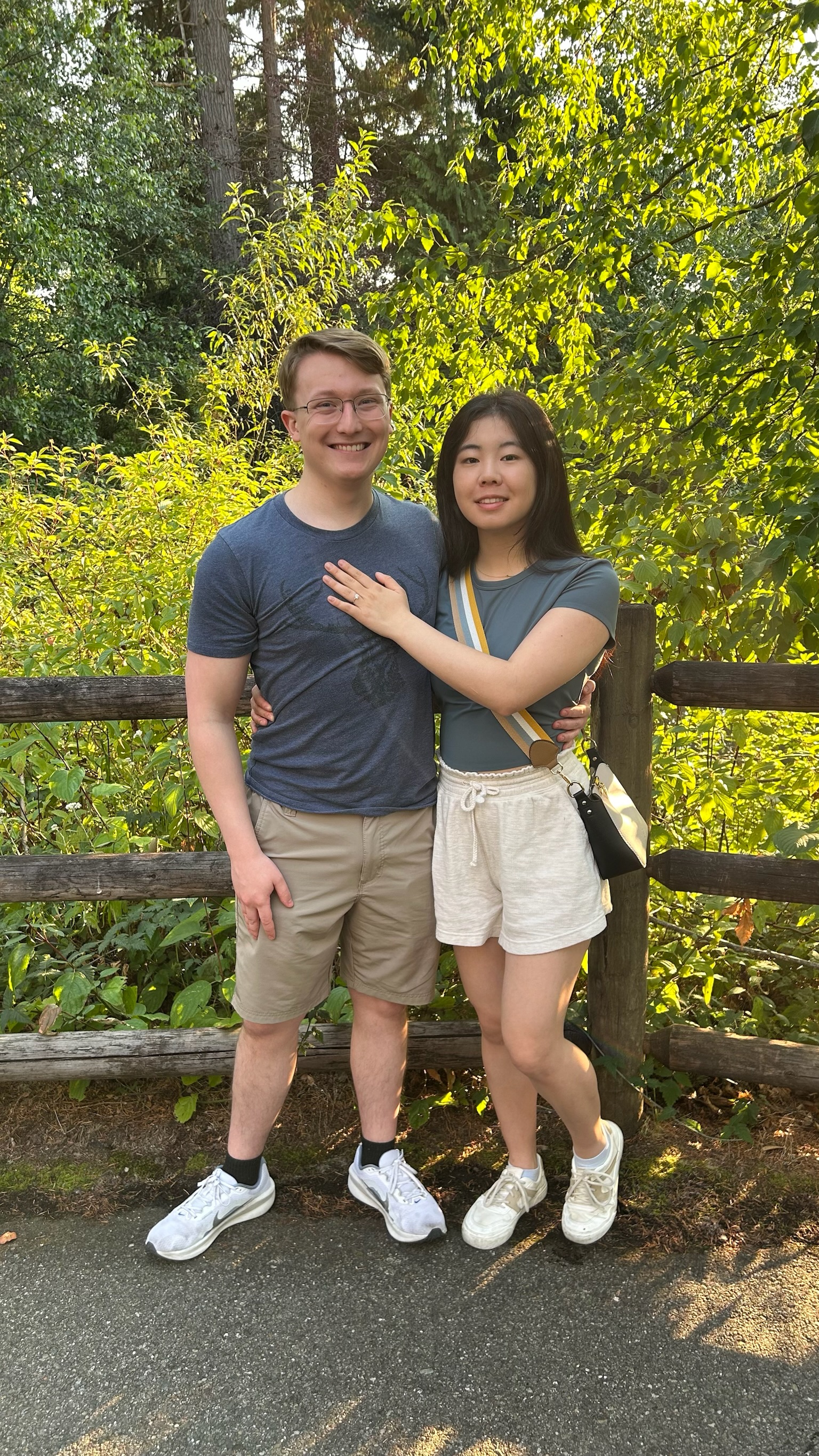 Angela showing her engagement ring while standing with Aidan in a leafy garden