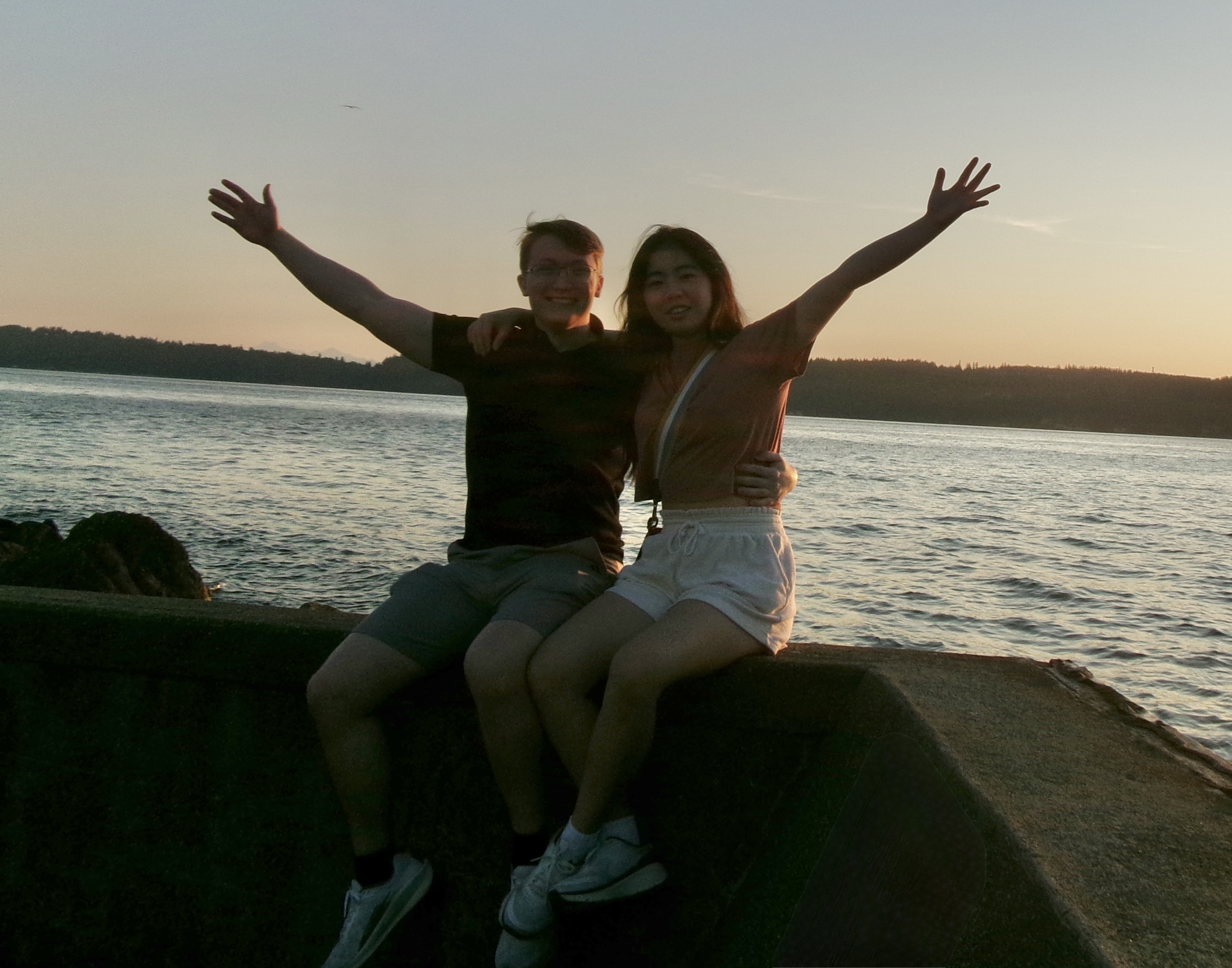 Angela and Aidan sitting by the water at sunset